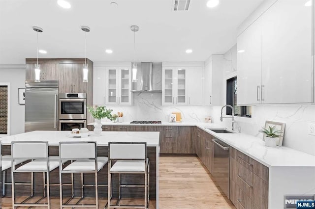 kitchen with white cabinetry, decorative light fixtures, a kitchen island, stainless steel appliances, and wall chimney range hood