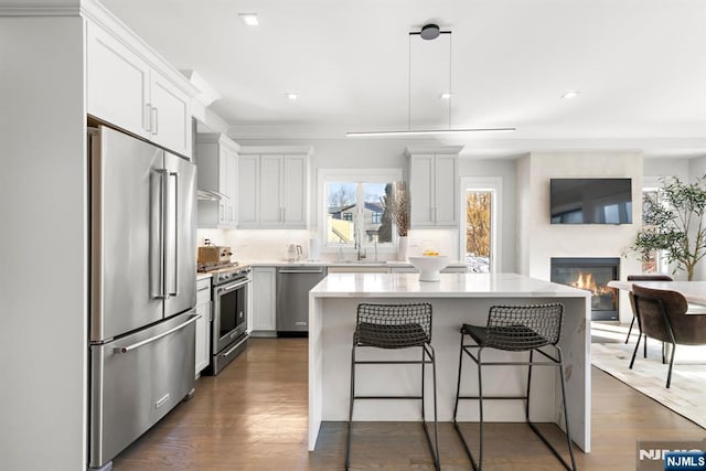 kitchen with high end appliances, white cabinetry, hanging light fixtures, dark hardwood / wood-style flooring, and a kitchen island