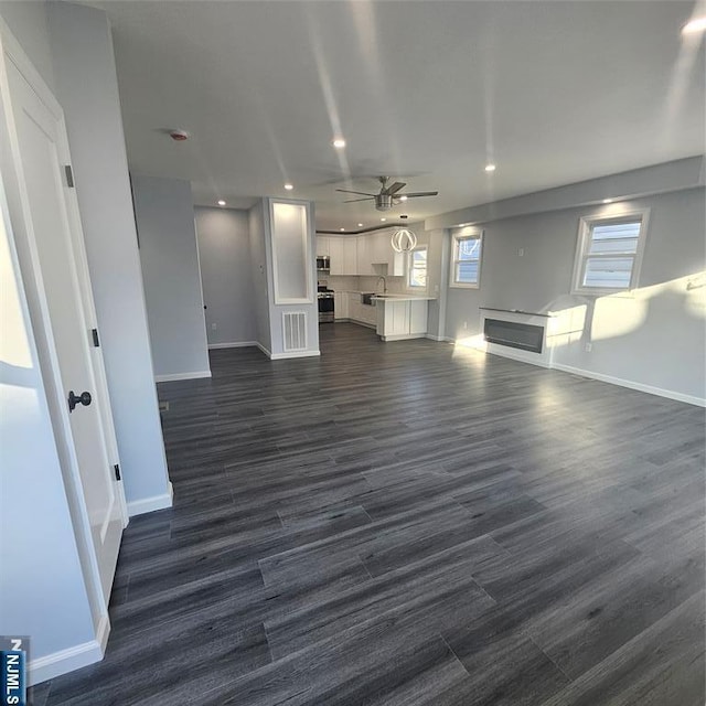 unfurnished living room featuring dark wood finished floors, recessed lighting, a sink, ceiling fan, and baseboards