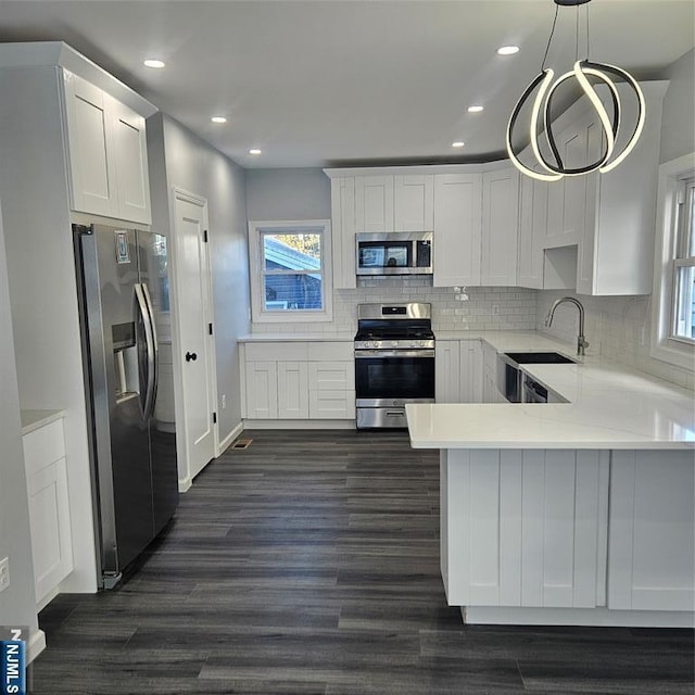 kitchen with appliances with stainless steel finishes, hanging light fixtures, white cabinets, dark hardwood / wood-style flooring, and kitchen peninsula