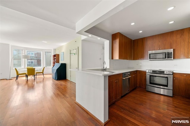 kitchen with backsplash, dark wood-type flooring, light countertops, brown cabinetry, and stainless steel appliances