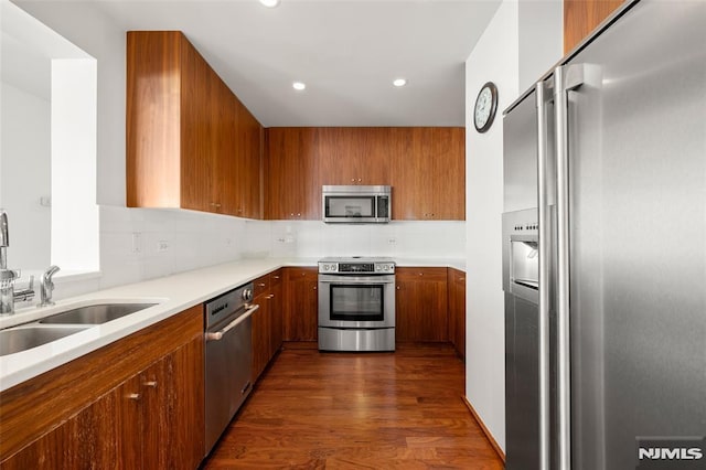 kitchen with brown cabinetry, dark wood finished floors, light countertops, appliances with stainless steel finishes, and tasteful backsplash