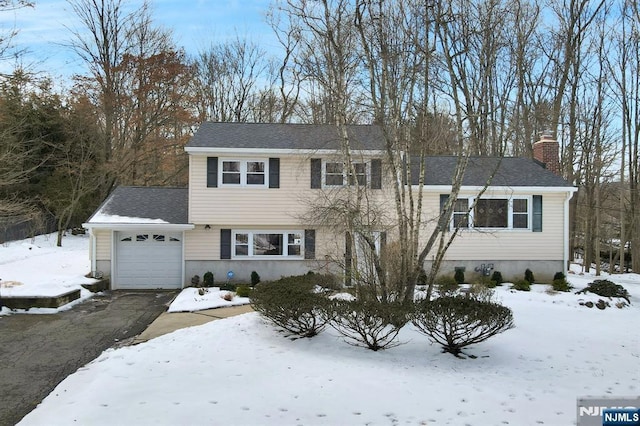 view of front facade featuring driveway, a chimney, an attached garage, and roof with shingles