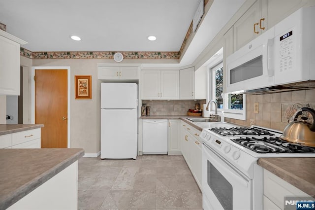 kitchen with light countertops, backsplash, white cabinets, a sink, and white appliances