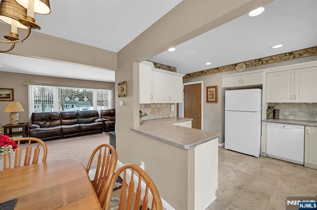 kitchen with a peninsula, white appliances, white cabinetry, open floor plan, and light countertops