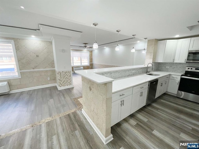 kitchen with appliances with stainless steel finishes, sink, white cabinetry, pendant lighting, and kitchen peninsula