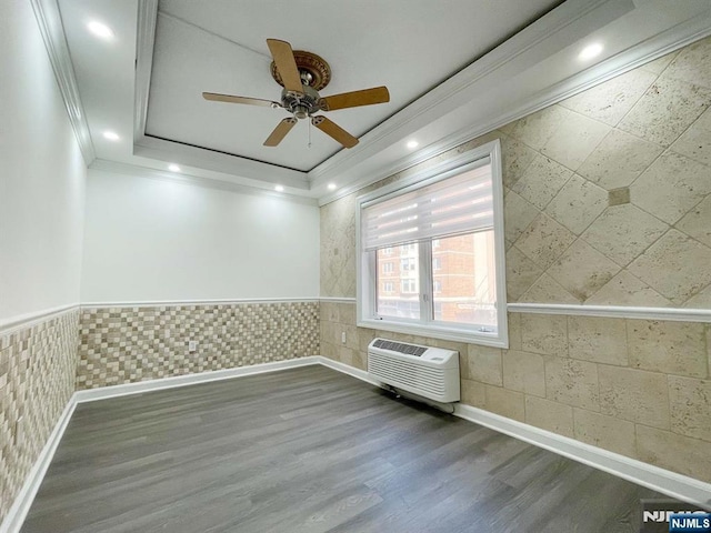 empty room featuring an AC wall unit, hardwood / wood-style flooring, a tray ceiling, ceiling fan, and crown molding