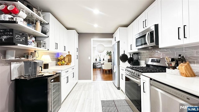 kitchen with stainless steel appliances, tasteful backsplash, white cabinets, and light hardwood / wood-style floors