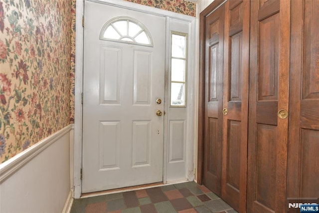 entryway with wallpapered walls, dark floors, and wainscoting