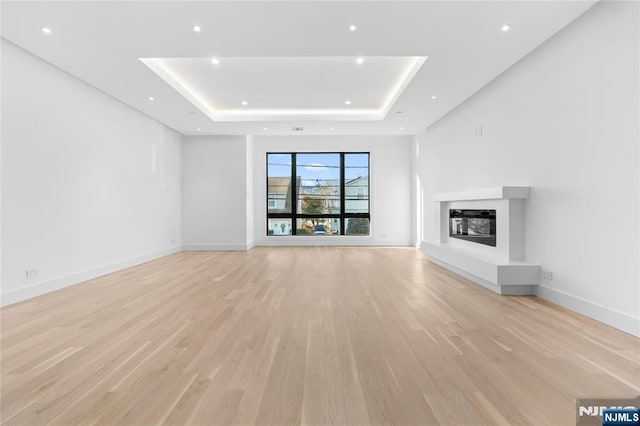 unfurnished living room with a raised ceiling and light hardwood / wood-style flooring