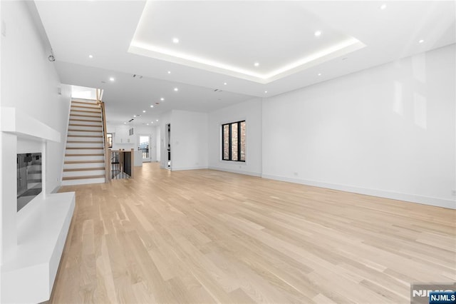 unfurnished living room featuring a tray ceiling and light hardwood / wood-style flooring