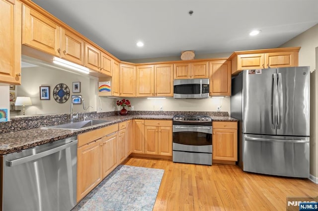 kitchen with stainless steel appliances, recessed lighting, a sink, dark stone countertops, and light wood-type flooring