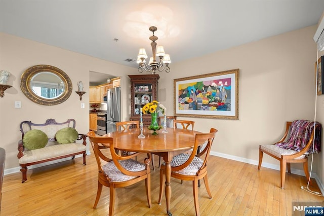 dining room with light wood finished floors, baseboards, visible vents, and a notable chandelier