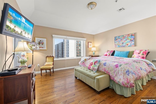 bedroom with wood finished floors, visible vents, and baseboards