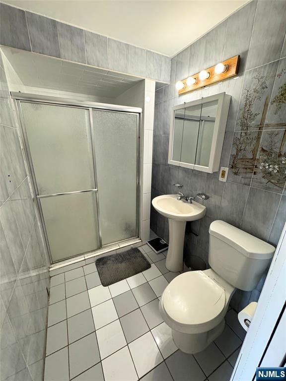 bathroom with toilet, tile walls, tile patterned floors, and a shower with shower door