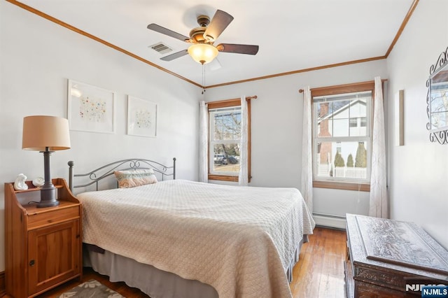 bedroom featuring ceiling fan, a baseboard heating unit, wood finished floors, visible vents, and crown molding