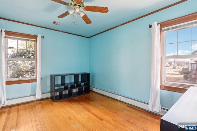 spare room featuring a baseboard heating unit, light wood-style floors, visible vents, and crown molding