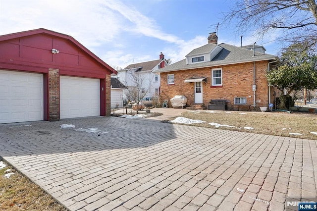 exterior space with a garage, a chimney, decorative driveway, an outdoor structure, and brick siding