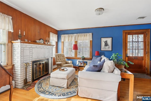 living room with a baseboard radiator, visible vents, ornamental molding, a brick fireplace, and wood finished floors