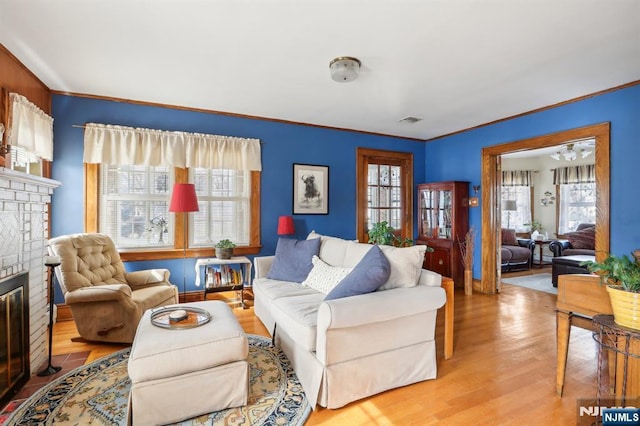 living room with crown molding, light wood-type flooring, visible vents, and a fireplace