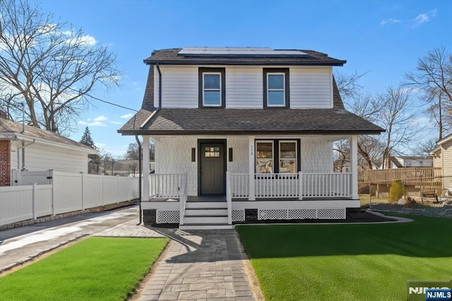 view of front of house with covered porch, roof with shingles, fence, and roof mounted solar panels