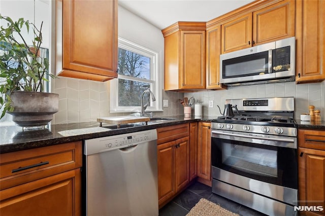 kitchen with sink, backsplash, stainless steel appliances, dark tile patterned flooring, and dark stone counters