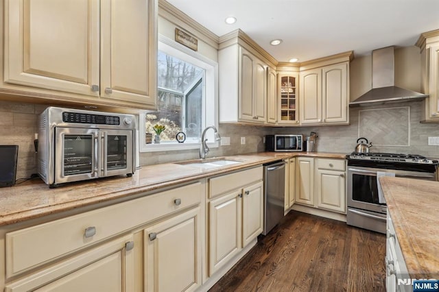 kitchen with stainless steel appliances, a sink, cream cabinets, and wall chimney exhaust hood