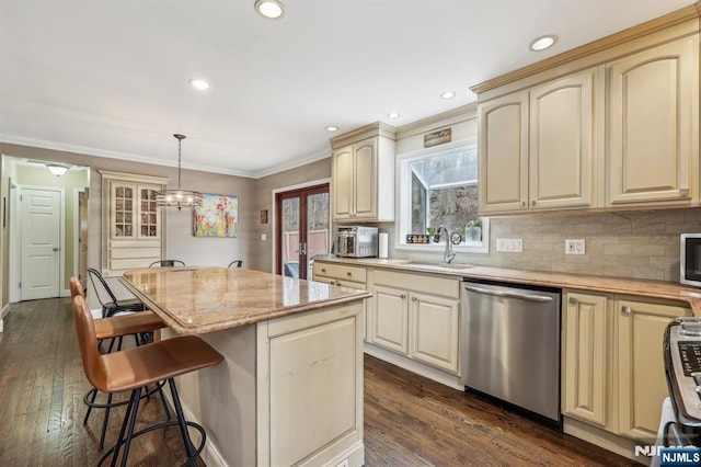 kitchen featuring a breakfast bar, a sink, cream cabinetry, stainless steel dishwasher, and a center island