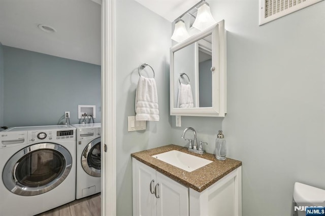 half bathroom with toilet, wood finished floors, vanity, visible vents, and washing machine and clothes dryer