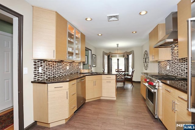 kitchen with kitchen peninsula, appliances with stainless steel finishes, light brown cabinetry, wall chimney exhaust hood, and pendant lighting