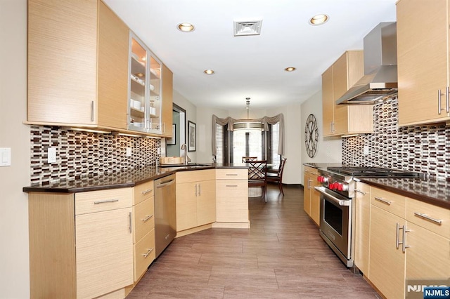 kitchen with light brown cabinetry, wall chimney range hood, and stainless steel appliances