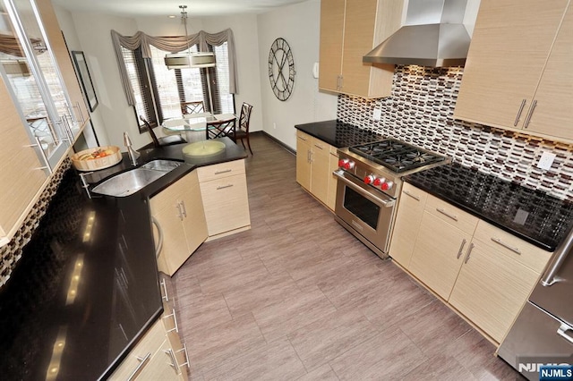 kitchen featuring sink, wall chimney exhaust hood, high end stove, light brown cabinets, and hanging light fixtures