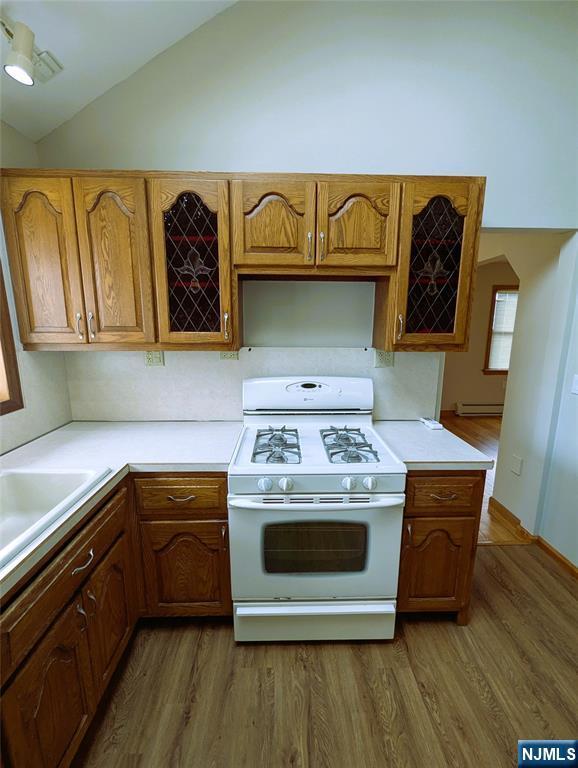 kitchen featuring lofted ceiling, light countertops, brown cabinetry, dark wood-type flooring, and white range with gas stovetop