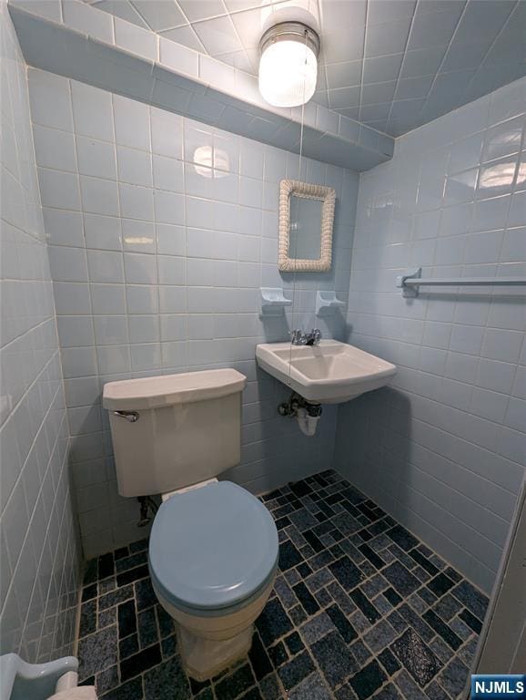 bathroom featuring a sink, tile walls, and toilet