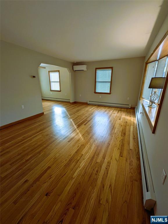 unfurnished living room with a baseboard radiator, an AC wall unit, and light wood-style flooring