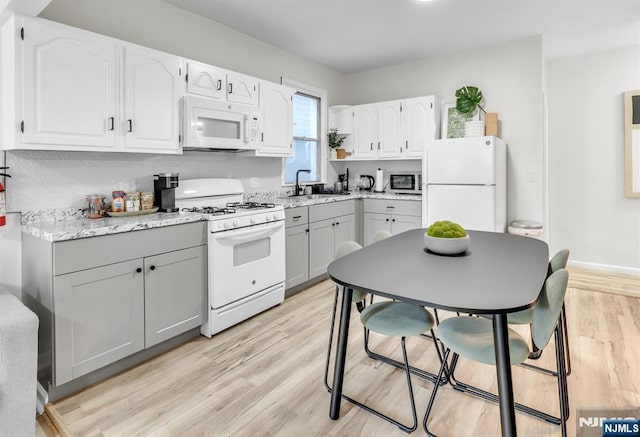 kitchen with sink, white appliances, light hardwood / wood-style floors, and white cabinets