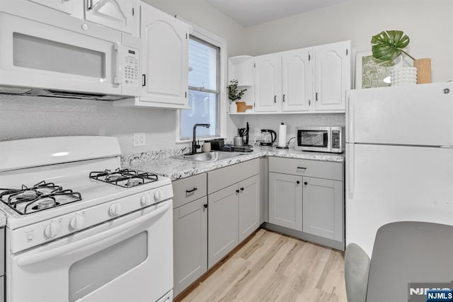 kitchen with sink, light wood-type flooring, white cabinets, light stone countertops, and white appliances