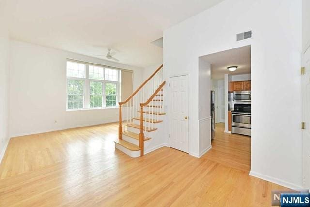 spare room featuring light wood finished floors, visible vents, baseboards, ceiling fan, and stairs