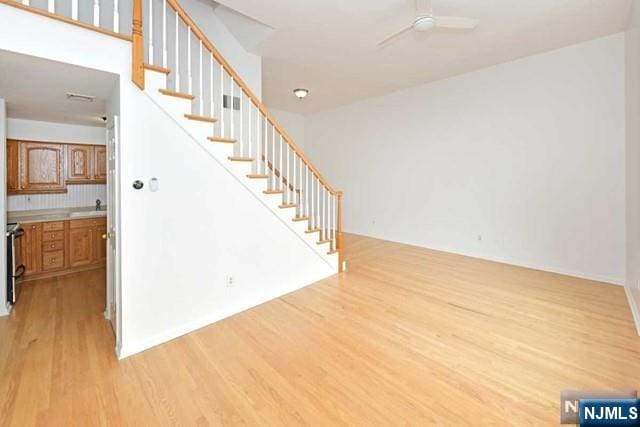 interior space featuring a ceiling fan, a sink, light wood finished floors, and stairs