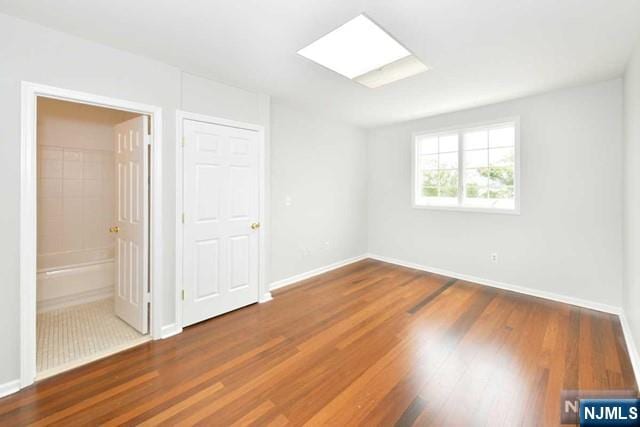 unfurnished bedroom featuring a skylight, ensuite bathroom, baseboards, and wood finished floors