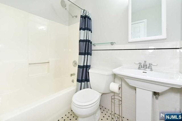 full bath with toilet, tile walls, shower / bath combination with curtain, and wainscoting