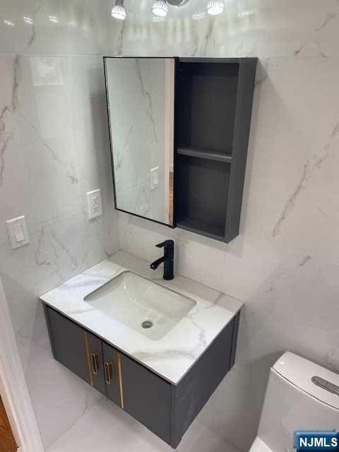 bathroom with tile walls, vanity, and toilet