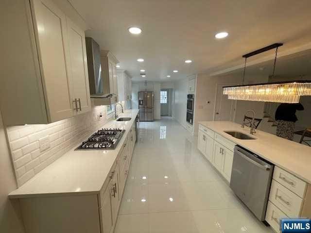 kitchen featuring white cabinetry, stainless steel appliances, decorative light fixtures, sink, and wall chimney range hood