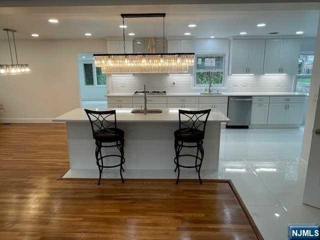 kitchen featuring decorative light fixtures, sink, dishwasher, white cabinets, and a breakfast bar area