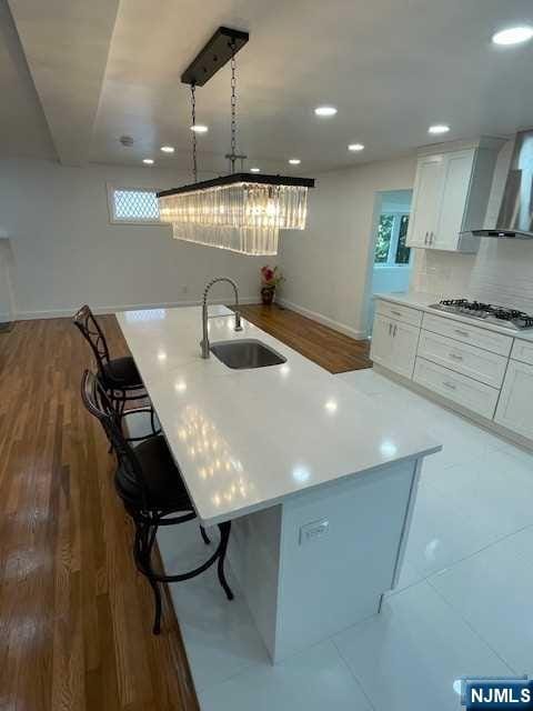 kitchen featuring sink, white cabinets, a breakfast bar, and wall chimney range hood