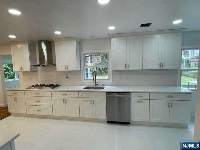 kitchen with wall chimney exhaust hood, stainless steel appliances, white cabinets, decorative backsplash, and sink