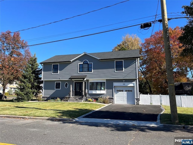 colonial-style house featuring a front yard, fence, driveway, and an attached garage