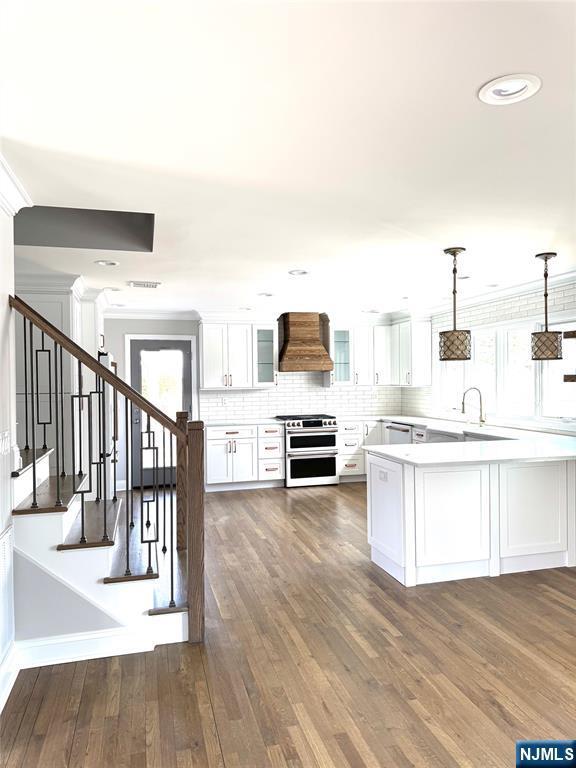 kitchen featuring premium range hood, white cabinetry, light countertops, hanging light fixtures, and double oven range