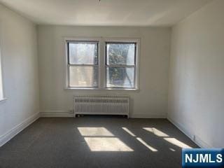 unfurnished room featuring radiator and baseboards