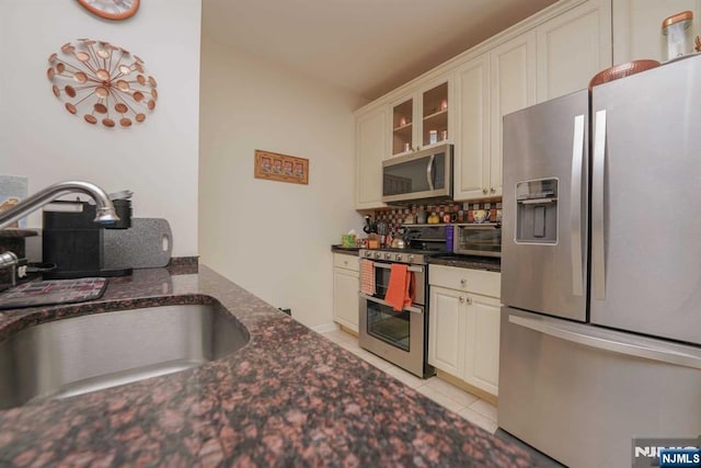 kitchen featuring sink, white cabinetry, light tile patterned floors, appliances with stainless steel finishes, and decorative backsplash